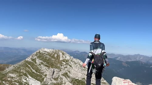 A Tourist with a Backpack on the Top of a Mountain Takes Off His Backpack and Spreads His Arms in a