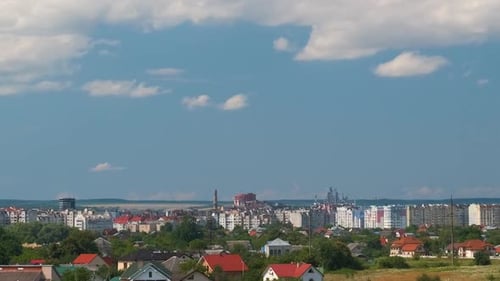 Zeitrafferaufnahmen von sich schnell bewegenden weißen, geschwollenen Cumuluswolken am blauen, klaren Himmel über kleinen Häusern in