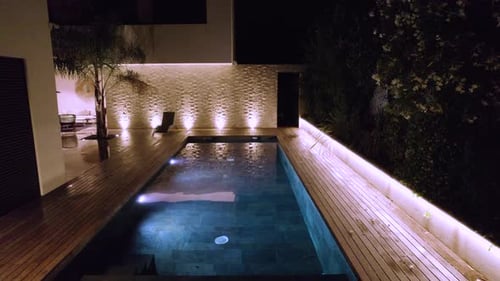 Langsame Luftaufnahme eines privaten Pools mit Unterwasserbeleuchtung bei Nacht