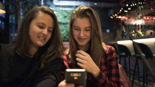 Two teenage girlfriends chatting and drinking cocktails in a trendy cafe
