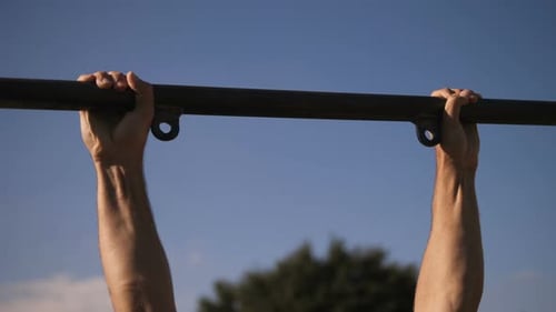 train outside - young man trains doing pull-ups at the bar