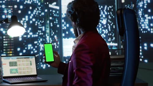 Man Looks at Phone at Desk in City at Night