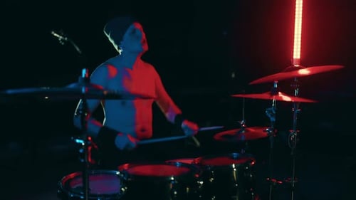 Man Energetically Playing Drums in Dark Studio with Lighting
