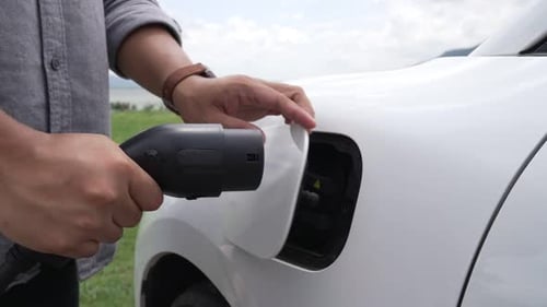 Progressiver Mann schließt Stromkabel an sein umweltfreundliches EV-Auto auf der grünen Wiese an