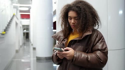 Focused African Female Waits for a Train in the Subway and Uses a Smartphone Surfs the Internet a