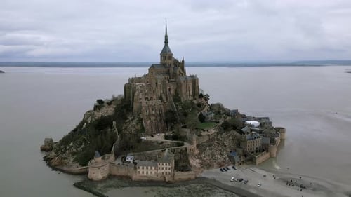 Mont Saint Michel during low tide on cloudy day, Normandy in France. Aerial orbiting