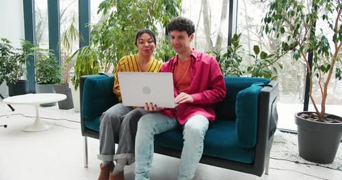 Confident Colleagues Sitting on Comfortable Sofa in Modern Office Having Video Call Waving Hand