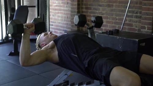 Tätowierter Mann im Fitnessstudio von der Seite geschossen beim Hantel-Brustdrücken