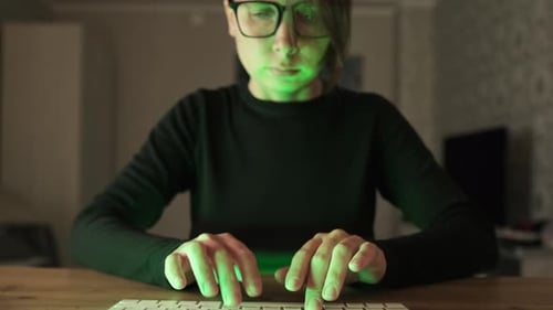 Une femme sérieuse à lunettes tape sur un clavier d'ordinateur portable moderne au feu vert. Travail tard dans la nuit