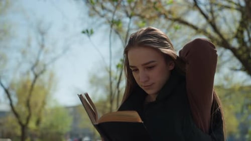 Young Woman Reads Book in Park on Sunny Day