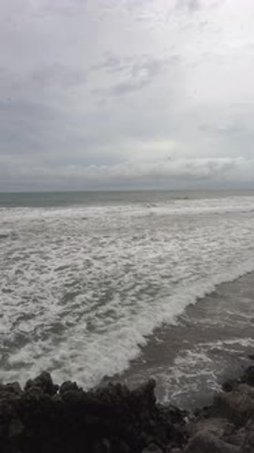 view of the beach, sea water accompanied by crashing waves, and coral rocks with a cloudy sky