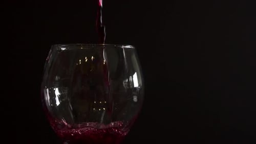 Pouring red wine into a glass, close up slow motion