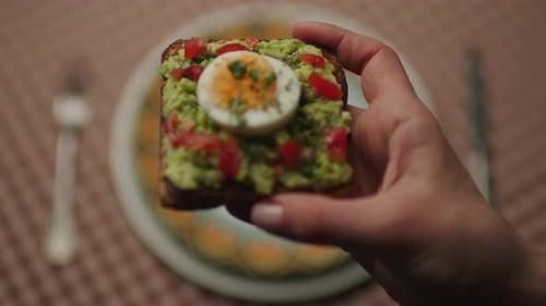 Hand Holding Avocado Toast With Egg Topping