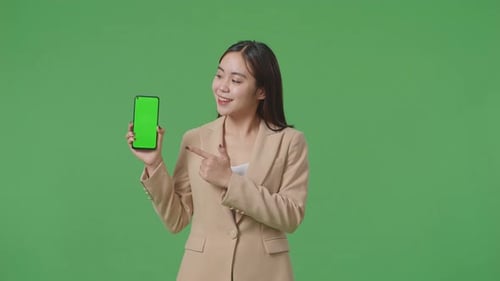Asian Business Woman With A Smile Showing And Pointing To Green Screen Mobile Phone On Green Screen