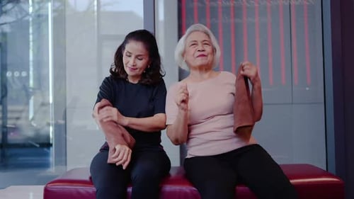 Active Asian senior women smiling and wiping sweat with towels after a fitness session at the gym.
