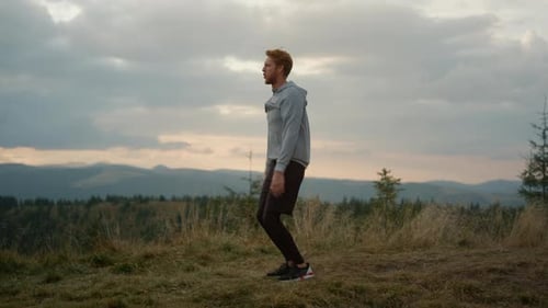 Young Runner Jumping on Place in Natural Landscape. Male Jogger Warming Before
