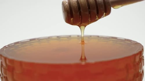 Honey Dripping from Wooden Dipper into Jar
