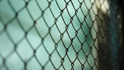 Nahaufnahme eines Maschendrahtzauns in scharfem Fokus vor einem leicht verschwommenen blaugrünen Hintergrund