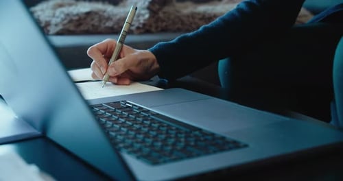 Person Writing in Notebook Next to Laptop