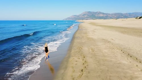 Woman walking in black swimsuit on sandy shore on beach along sea