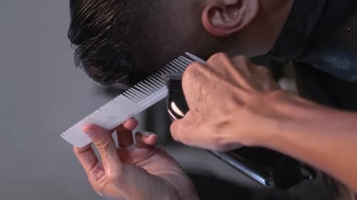 White comb and battery powered hair clipper used to trim and level edges of black hair on rear right