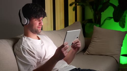 Young Man Uses Tablet with Headphones Indoors