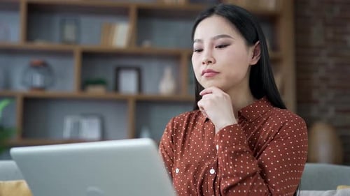 Serious young asian businesswoman works on laptop sitting in home office.