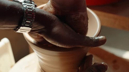 Close-Up of Two Men's Hands Shaping Pottery on Wheel During Lesson in Sunlit Studio