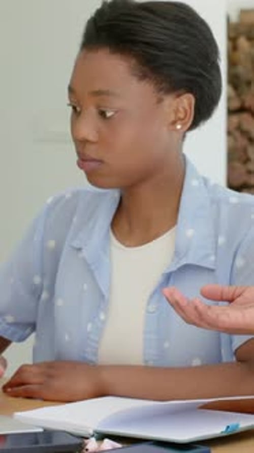 Vertical video: Student at wood table watching adult hand entering and pointing at notes for study