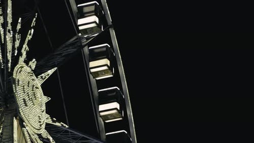 Illuminated modern Ferris wheel with enclosed cabins, slowly moving in the light of the night lights