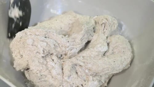 Close-up of a hand with a spatula vigorously mixing bread dough in a bowl, capturing the initial and