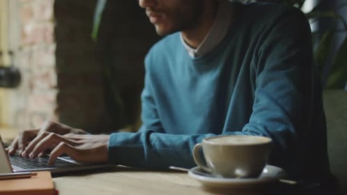 Man Types on Laptop With Coffee in Cafe