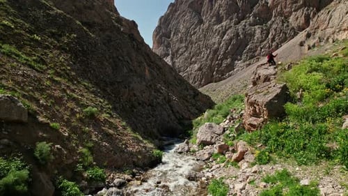 Woman Sitting by the Flowing River in the Mountain