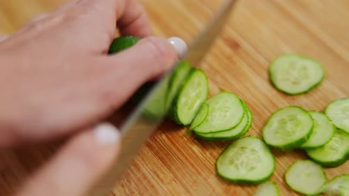 High Angle View Closeup Female Hand Slicing Cucumber with Knife on Cutting Board Closeup