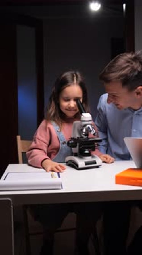 Girl and Man Look Through a Microscope Together