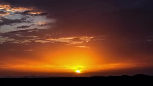 Timelapse View Of Golden Orange Sun Rays Flowing Out Through Cloudscape Over Silhouetted Landscape.