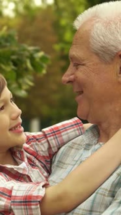 Child Hugging Grandfather in a Green Urban Park