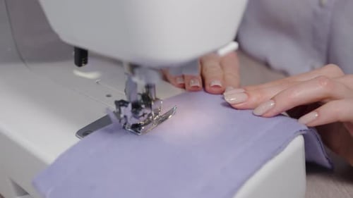 Closeup View of a Seamstress Skillfully Sewing Purple Fabric on a Sewing Machine The Focus