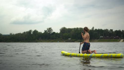 Man Paddleboarding on Lake Kneeling Down