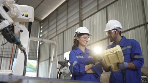 Blue collar workers at machine shop with welding robot arm.