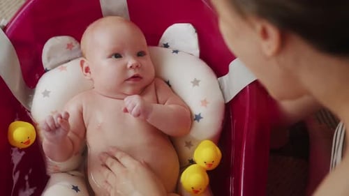 Mother Bathes Her Baby in Pink Bathtub Top View