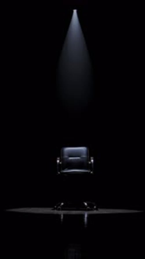 Silla de oficina solitaria iluminada por un foco en un cuarto oscuro