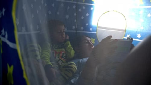 Slow motion of a young mexican latin mother reading a book to her son inside his blue castle tent we