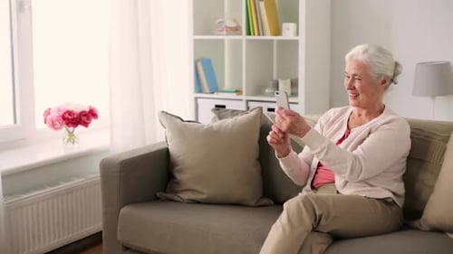 Smiling Senior Woman Using Smartphone on Couch at Home