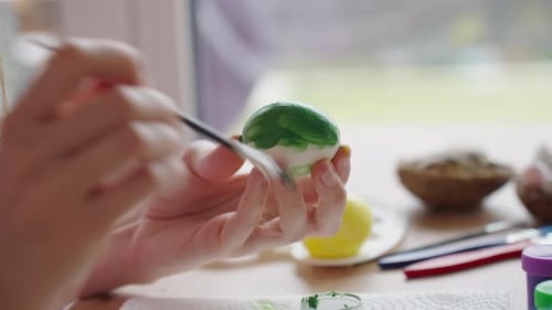 Woman painting Easter egg with green paint and brush
