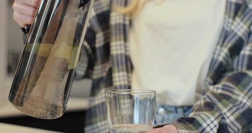 Young Woman Pours and Drinks Lemon Water