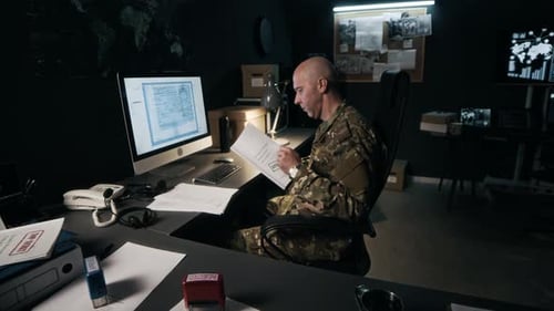 Commander Answering Phone Working with Papers in front of Computer in Office