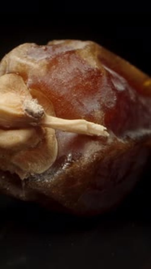 Dried dates on a black table with a mirror image. Dolly slider extreme close-up. Vertical video.