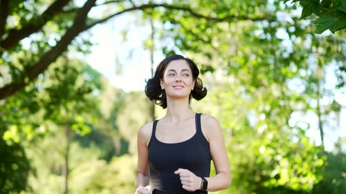 Young female runner jogging in an urban city park. Happy brunette sportswoman enjoys jogging outdoor