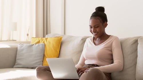 Young Carefree African American Woman Chatting with Friends Online Typing on Laptop at Home Tracking